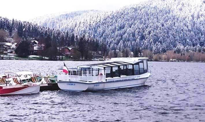 Grand bateau péniche blanc au milieu du lac de Gérardmer avec fond de sapin blanc
