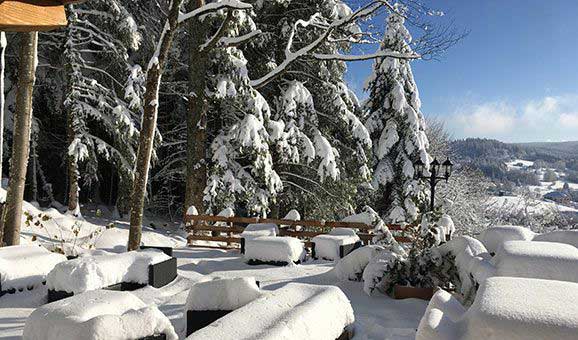 Terrasse et table sous la neige avec les sapins et le ciel bleu