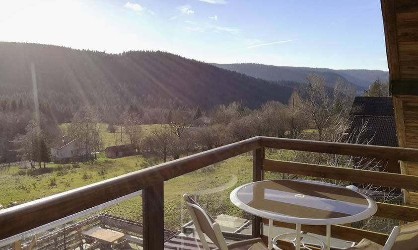 Petit balcon en bois avec table et chaise, donnant sur les montagnes vosgiennes et la vallée sous le soleil